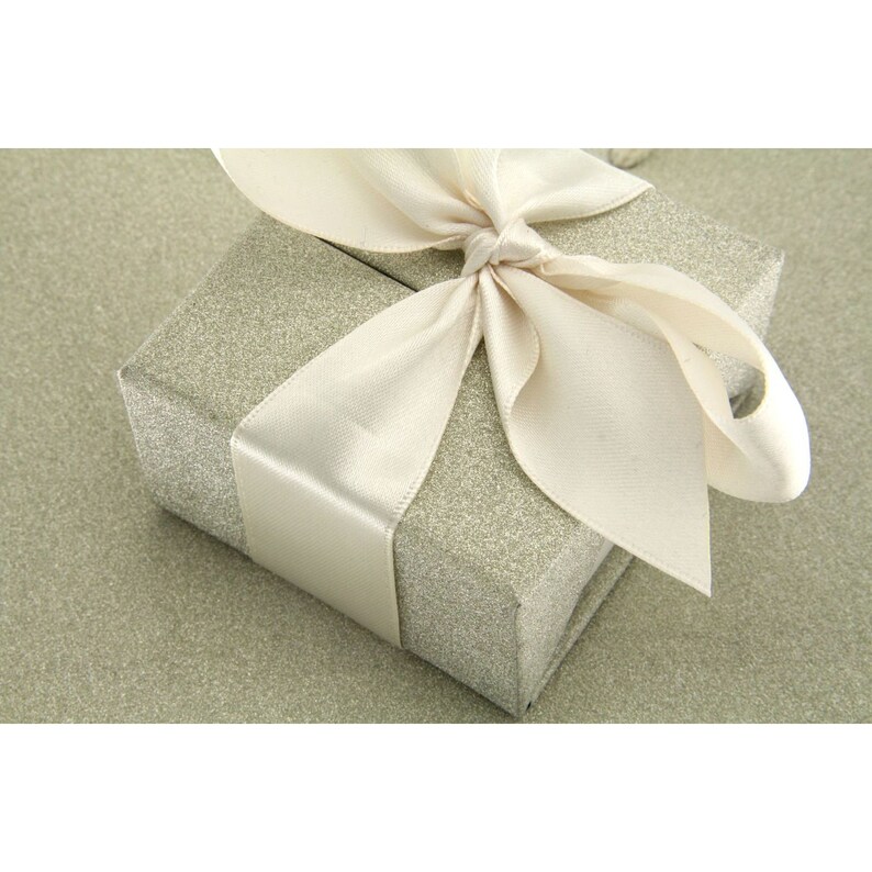 May include: A small, silver gift box with a white satin ribbon tied in a bow. The box is sitting on a textured, silver background.
