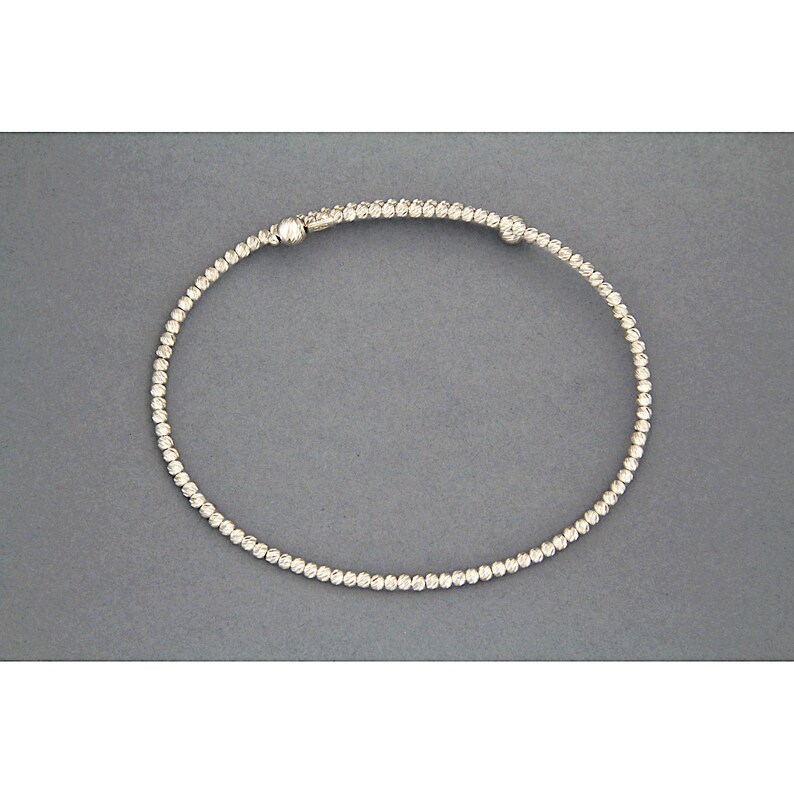 May include: A silver bracelet with a textured design and small round beads.