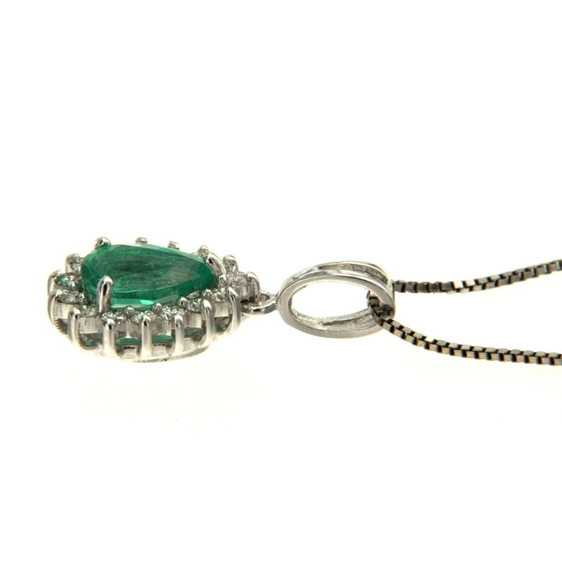 May include: A pear-shaped emerald gemstone pendant set in a white gold halo with smaller diamonds. The pendant is attached to a delicate silver chain.