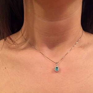 May include: A silver chain necklace with a teardrop-shaped pendant featuring a green gemstone surrounded by smaller clear gemstones.