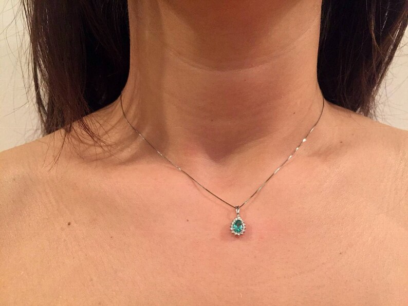 May include: A silver chain necklace with a teardrop-shaped pendant featuring a green gemstone surrounded by smaller clear gemstones.