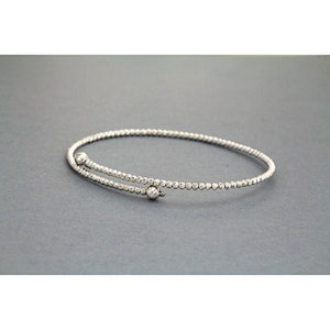 May include: A silver bangle bracelet with a textured design and two small round accents.