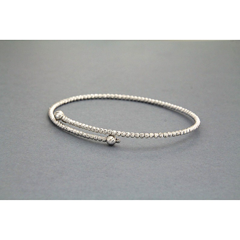 May include: A silver bangle bracelet with a textured design and two small round accents.