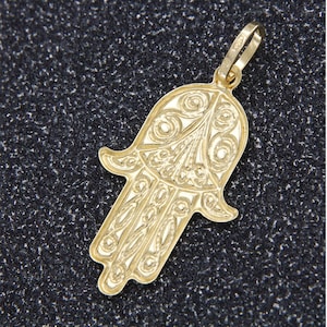 Könnte beinhalten: Ein goldfarbener Anhänger in Form einer Hamsa-Hand, ein Symbol für Schutz und Glück. Der Anhänger ist aufwendig mit einem floralen Muster verziert.