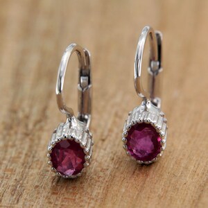 Puede incluir: Un par de pendientes de aro de plata con una piedra preciosa rosa en el centro de cada pendiente.
