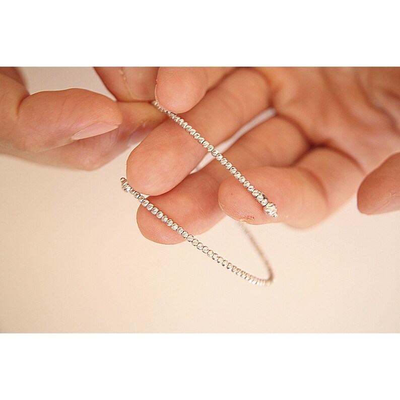 May include: A silver beaded bracelet with a delicate design. The bracelet is made of small, round beads that are evenly spaced.