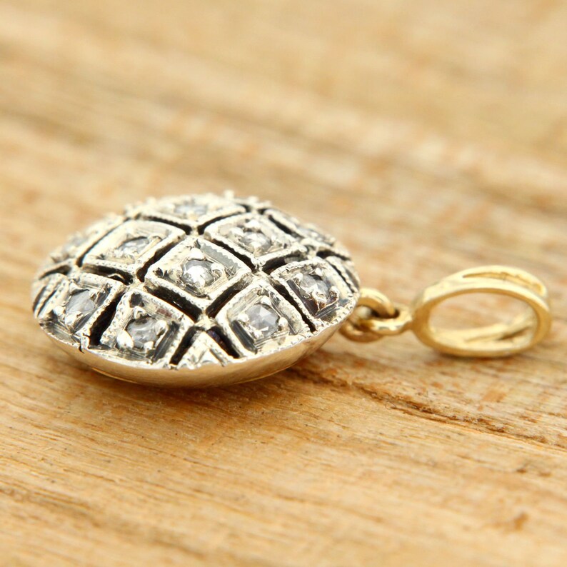 Pode incluir: Um pingente de prata com um design redondo e geom&eacute;trico cravejado com pequenos diamantes. O pingente est&aacute; preso a uma corrente de ouro.