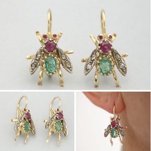 May include: Gold fly earrings with ruby and emerald details. The earrings have a detailed insect design, with ruby eyes, emerald bodies, and diamond-set wings. Multiple views of the earrings are shown.
