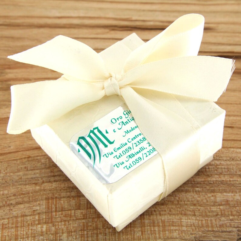Pode incluir: Uma pequena caixa de presente branca com uma fita de cetim branca amarrada em um la&ccedil;o. A caixa tem um r&oacute;tulo prateado com texto verde que diz "DM Oro Gi e Antig Moden Via Emilia Centro Tel.059/2358 Via Albinelli, 2 Tel.059/2208".