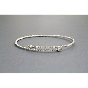 May include: A silver bangle bracelet with a textured finish and two small round beads at the clasp.