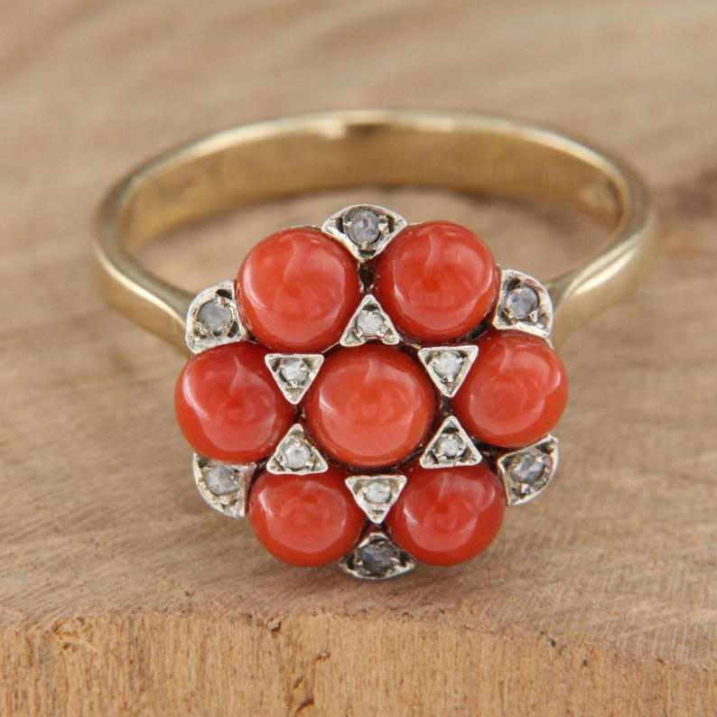 May include: A gold ring with a cluster of red coral stones and small diamonds set in a flower shape.