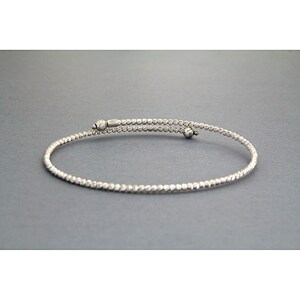 May include: A silver bangle bracelet with a textured finish. The bracelet is open and has a small ball at each end.