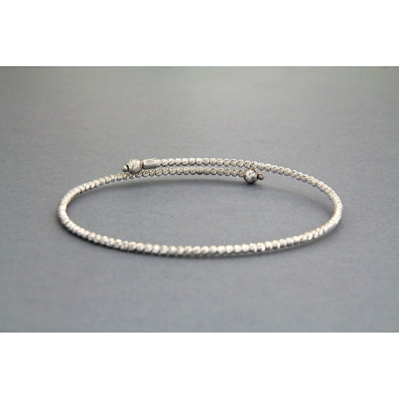 May include: A silver bangle bracelet with a textured finish. The bracelet is open and has a small ball at each end.