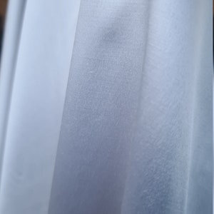 Peut inclure: Gros plan sur un tissu blanc avec une texture lisse et soyeuse. Le tissu est plié et drapé, créant des plis et des plis doux.