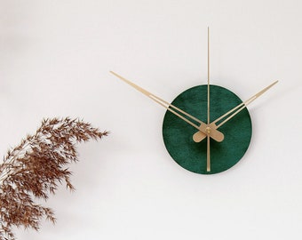Puede incluir: Un reloj redondo verde con manecillas doradas en una pared blanca. Un jarrón con hierba marrón seca está sobre una superficie blanca. Una cómoda blanca con cuatro cajones tiene una pila de libros y una bola de papel marrón en la parte superior. El libro tiene el texto "OGILVY ON ADVERTISING" impreso en la portada.