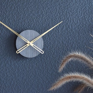 May include: A gold clock with a gray face and black hands against a blue textured wall.