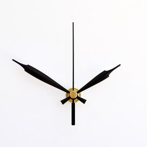 Può includere: Lancette dell'orologio nere con un centro dorato, su uno sfondo bianco.