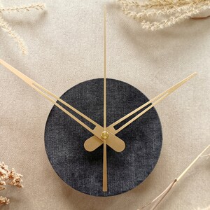 May include: A black and gold clock with a round face and gold hands. The clock is set against a light beige background.