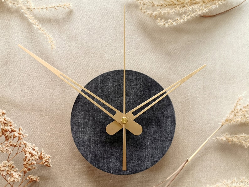 May include: A black and gold clock with a round face and gold hands. The clock is set against a light beige background.