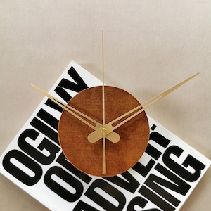 May include: A brown wooden clock with gold hands on a white background with black text that reads " Ogilvy & Mather Advertising ".