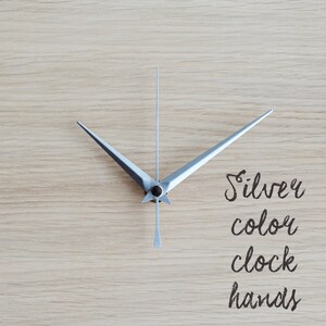 May include: Silver clock hands on a light wood background. The text "Silver color clock hands" is written below the hands.