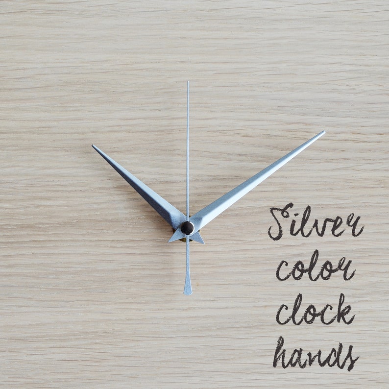 May include: Silver clock hands on a light wood background. The text "Silver color clock hands" is written below the hands.
