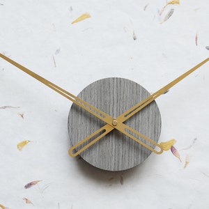 May include: A gray wood clock with gold hands. The clock is round and has a simple design.