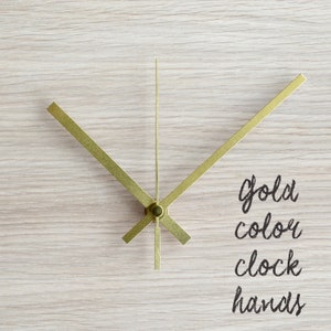 May include: Gold-colored clock hands on a light wood background. The text "gold color clock hands" is written below the hands.