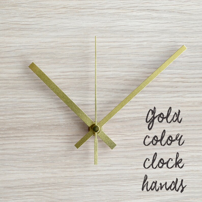 May include: Gold-colored clock hands on a light wood background. The text "gold color clock hands" is written below the hands.