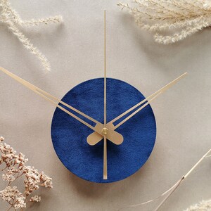 May include: A blue round clock with gold hands on a beige background.