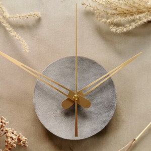 May include: A gray circular clock face with gold hands. The clock is mounted on a beige wall with dried flowers on either side.