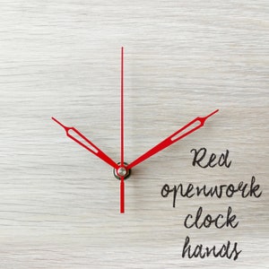 May include: Red openwork clock hands on a light wood background.