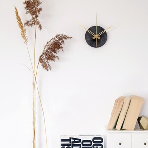 May include: A black and gold clock with thin gold hands on a white wall. A dried grass arrangement is in a clear vase on a white surface. A white dresser with four drawers has a stack of books and a brown decorative object on top. The book is titled "Ogilvy on Advertising".