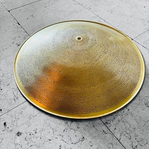 Pode incluir: Um abajur de metal dourado com forma circular e abobadada com um pequeno furo no centro. O abajur é coberto com um padrão de pequenos furos espaçados uniformemente.
