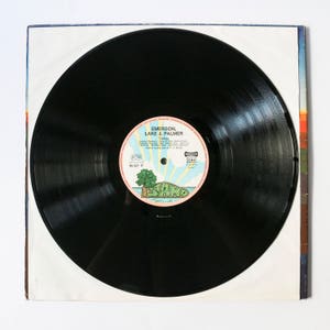 Pu&ograve; includere: Disco in vinile nero con un'etichetta bianca che presenta il testo "Emerson, Lake & Palmer" e il titolo dell'album "Tarkus". L'etichetta include anche il testo "Island" e un logo di una palma su un'isola.