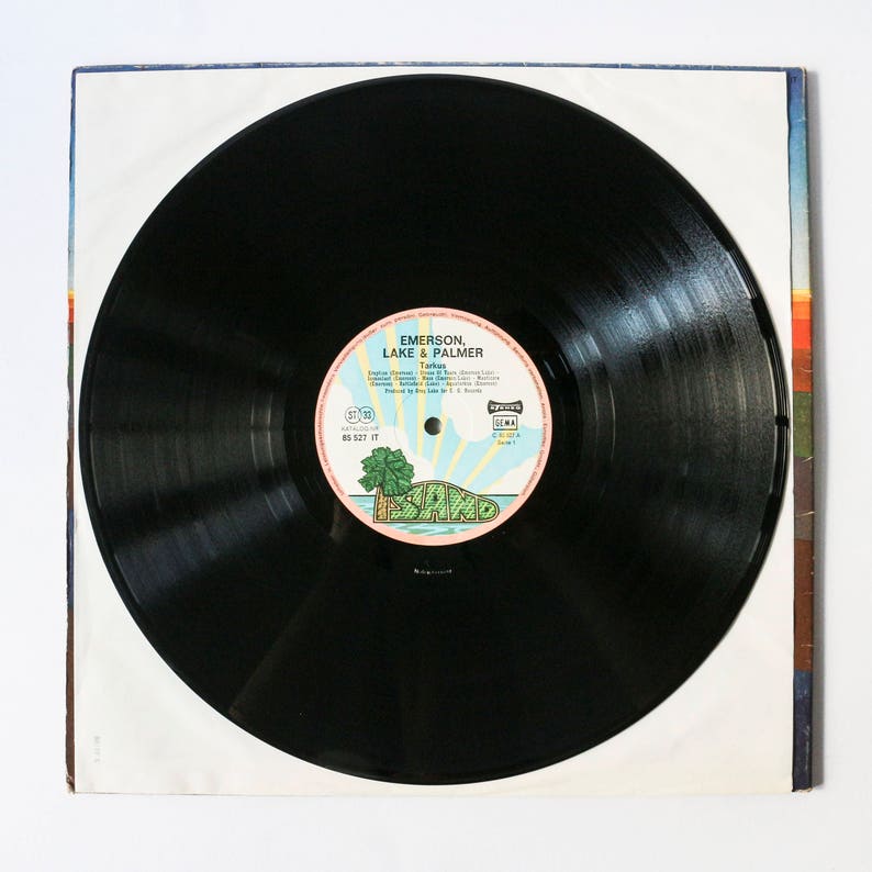 Pu&ograve; includere: Disco in vinile nero con un'etichetta bianca che presenta il testo "Emerson, Lake & Palmer" e il titolo dell'album "Tarkus". L'etichetta include anche il testo "Island" e un logo di una palma su un'isola.