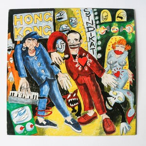 Könnte beinhalten: Eine farbenfrohe Illustration einer Band mit dem Text "Hong Kong" und "Syndikat" auf dem Cover. Die Bandmitglieder tragen rote, blaue und schwarze Kleidung. Die Illustration ist im Cartoon-Stil mit kräftigen Linien und leuchtenden Farben gehalten.