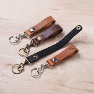 May include: Three leather keychains with metal key rings. The keychains are brown, black and tan. The brown keychain has the initials "E+A" engraved on it. The black keychain has a silver ring. The tan keychain has the initials "RC" engraved on it.