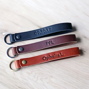 May include: Three leather keychains with different engravings. The top keychain is black and engraved with "09.30.17". The middle keychain is brown and engraved with "PFL". The bottom keychain is brown and engraved with "Ophelia L."