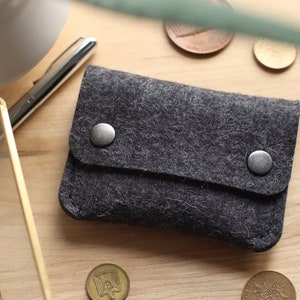 May include: A gray felt wallet with two silver snaps. The wallet is on a wooden surface.