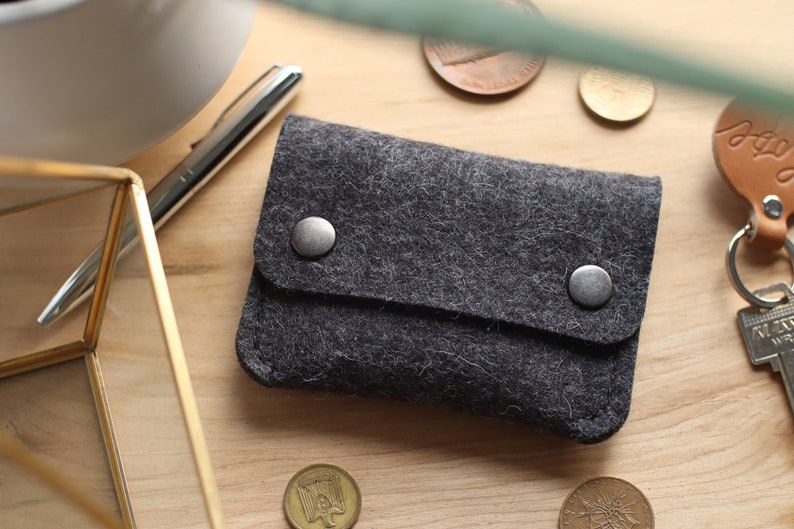 May include: A gray felt wallet with two silver snaps. The wallet is on a wooden surface.