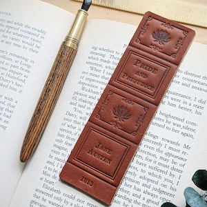 May include: A brown leather bookmark with embossed details. The bookmark features the title "Pride and Prejudice" by Jane Austen, along with a decorative floral design and the publication date "1813".