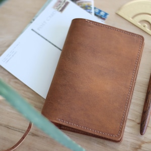 May include: A brown leather journal with stitched edges, lying on a wooden surface with a pen and a gold protractor.