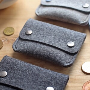 May include: Three gray felt pouches with a flap closure and metal snaps. The pouches are arranged in a row on a wooden surface.