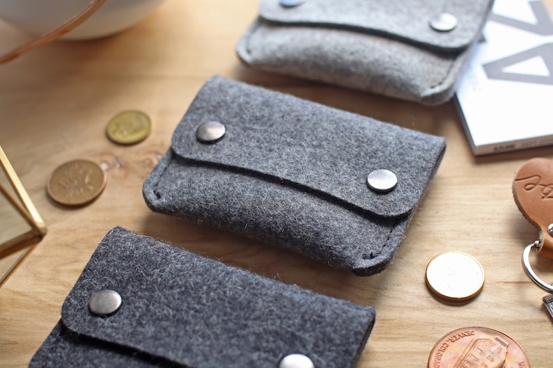 May include: Three gray felt pouches with a flap closure and metal snaps. The pouches are arranged in a row on a wooden surface.