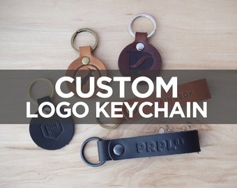 May include: Four leather keychains with custom logos. The keychains are in different colors and styles, including a round keychain with a black logo, a round keychain with a brown logo, a round keychain with a brown logo, and a rectangular keychain with a black logo.