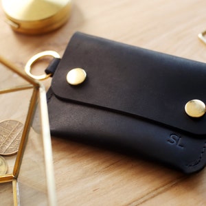 May include: A black leather wallet with gold accents and the initials "SL" embossed on the front.