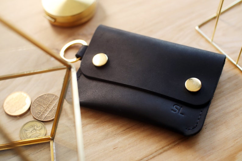May include: A black leather wallet with gold accents and the initials "SL" embossed on the front.