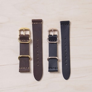 Puede incluir: Tres correas de reloj de cuero con hebillas doradas. Las correas son marrón, negro y negro.