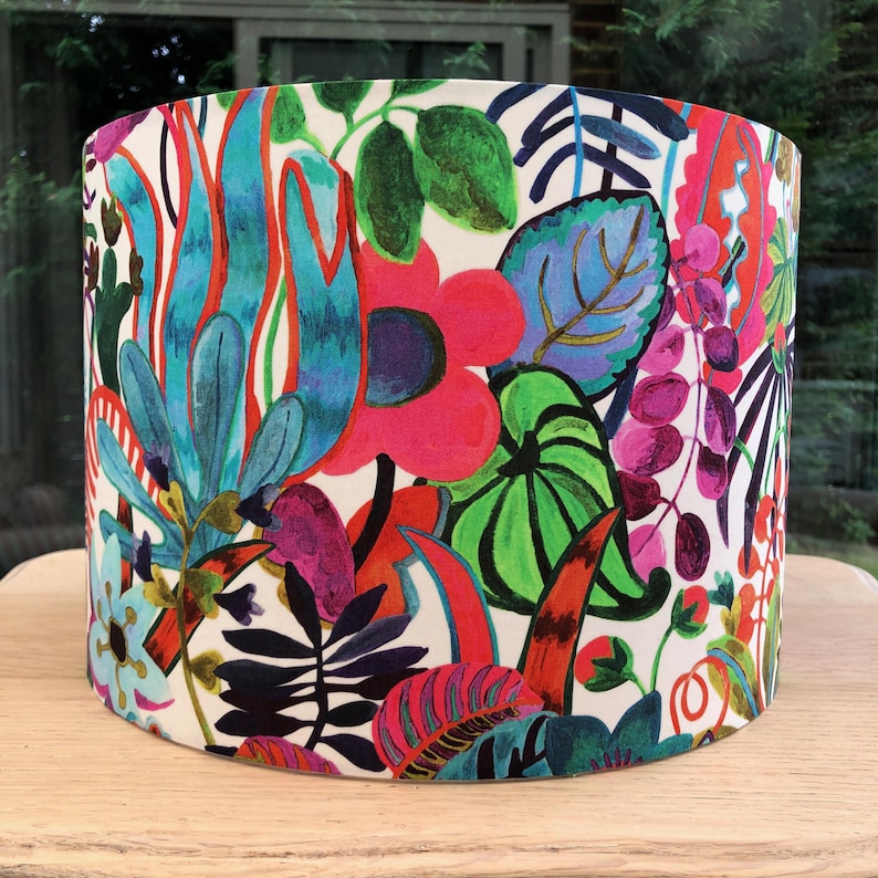 K&ouml;nnte beinhalten: Ein zylindrischer Lampenschirm mit einem lebendigen Blumenmuster. Das Design zeigt gro&szlig;e, farbenfrohe Blumen und Bl&auml;tter in Pink-, Blau-, Gr&uuml;n- und Rott&ouml;nen auf wei&szlig;em Hintergrund. Der Lampenschirm ist aus Stoff und eignet sich f&uuml;r eine Tisch- oder Stehlampe.